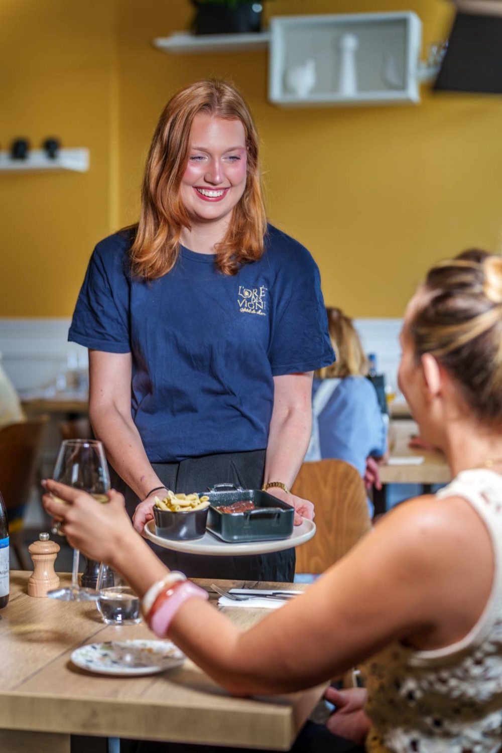 Serveuse souriante présentant un plat de viande mijotée et pâtes au Bistrot de l'O